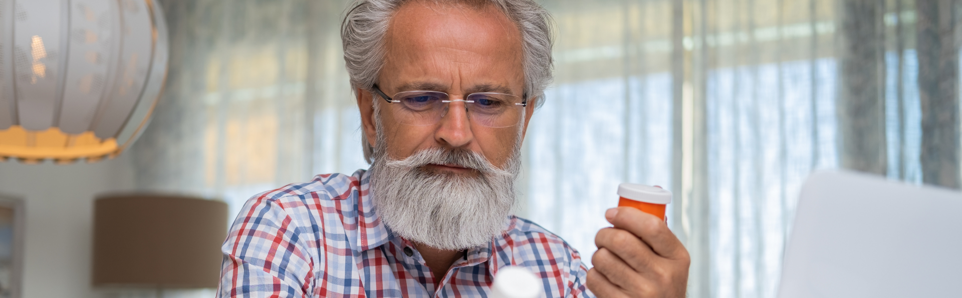 Grey haired man with beard holding pill bottle